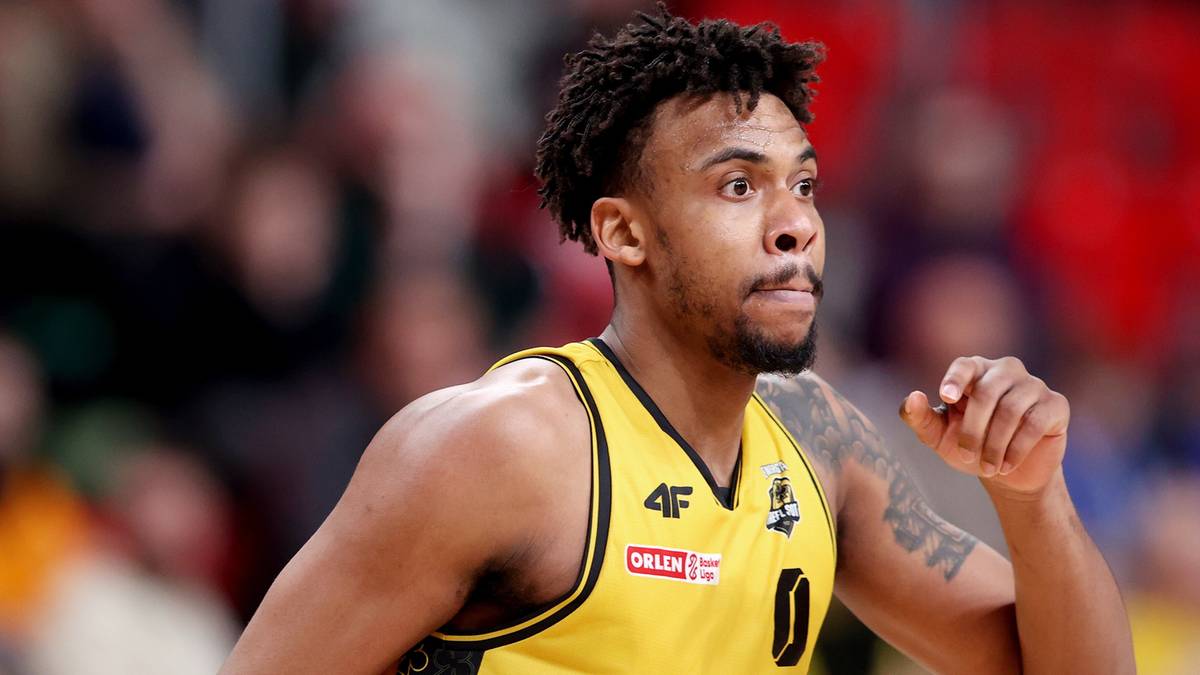 Koszykarz w żółtej koszulce podczas meczu, z widocznym numerem 0 i logotypami sponsorów.