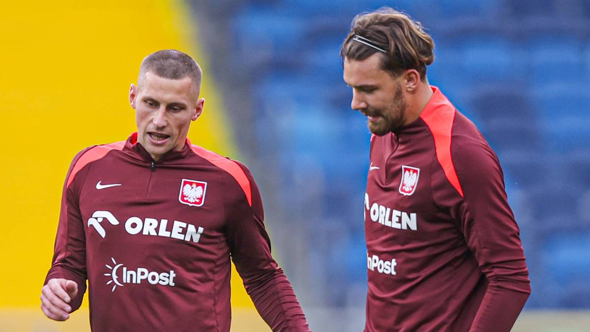 Piłkarze reprezentacji Polski w bordowych strojach treningowych stoją na boisku.