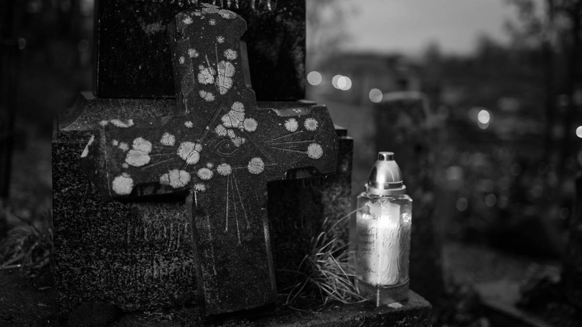 Kamienny nagrobek w kształcie krzyża ze światłem znicza.