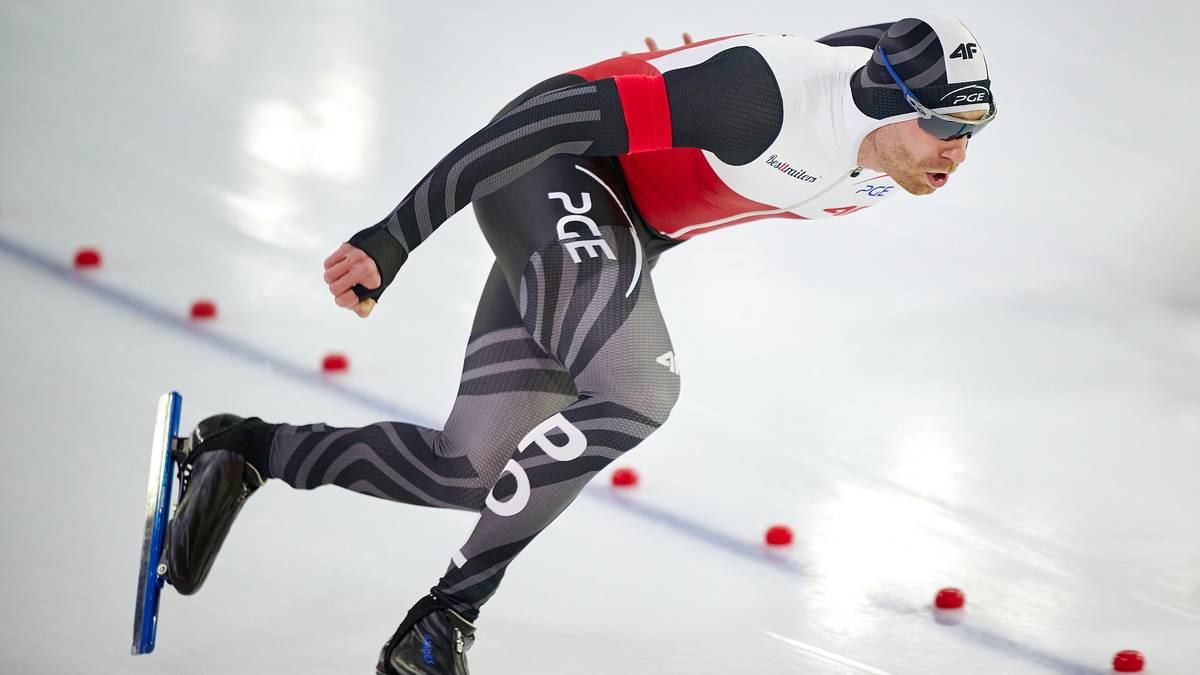 Łyżwiarz szybki w kombinezonie ślizga się po lodowym torze podczas zawod&oacute;w.