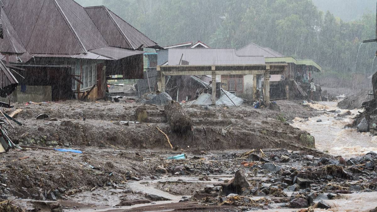 Budynki zniszczone przez powódź i osuwisko, zalanymi błotem i gruzem, w tle wzgórza pokryte zielenią.