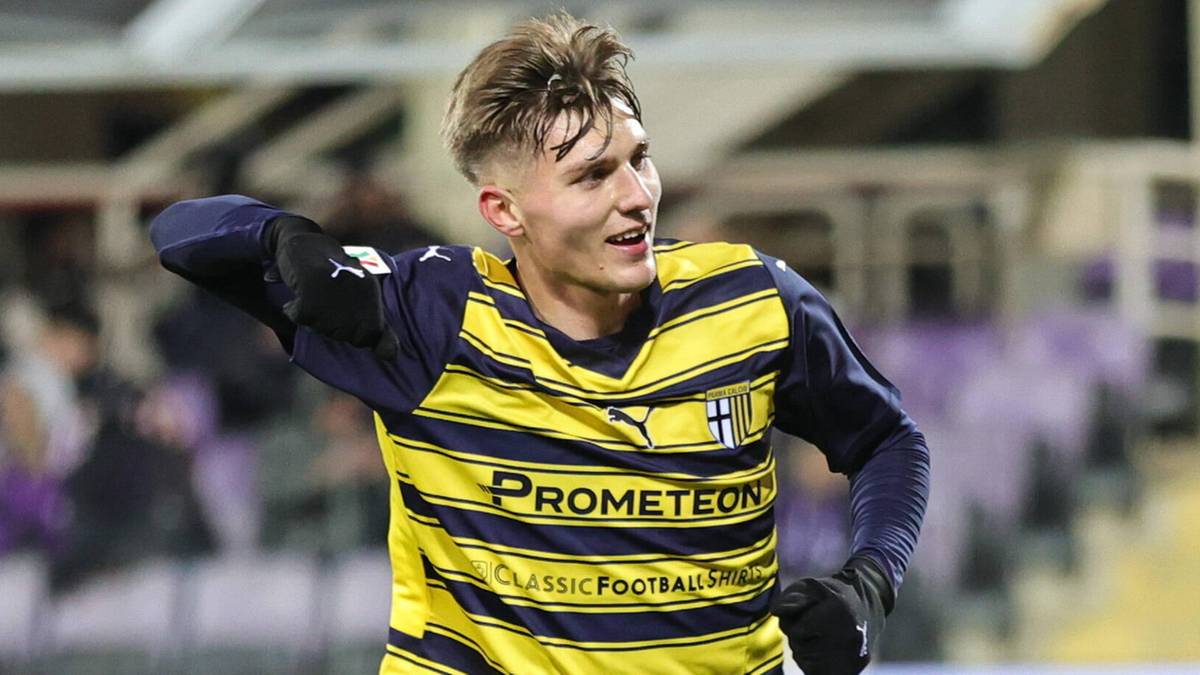 Młody piłkarz w żółto-niebieskiej koszulce, z uniesioną prawą ręką, celebruje bramkę lub zwycięstwo.