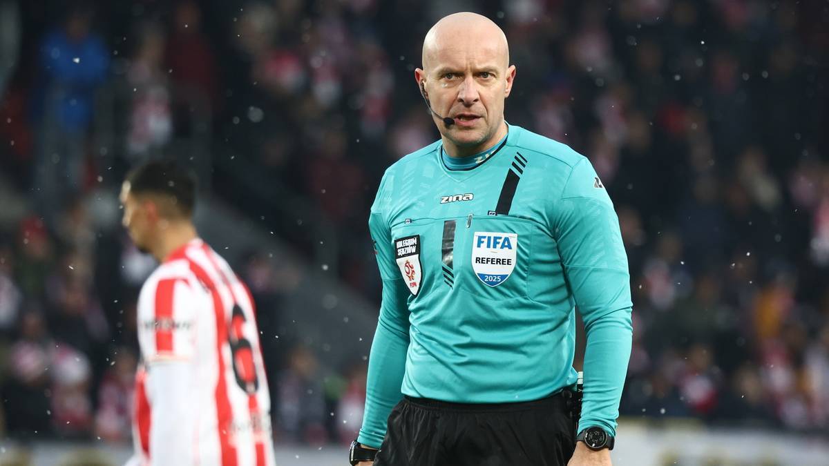 Szymon Marciniak w zielonej koszulce sędziego z logo FIFA i naszywkami.