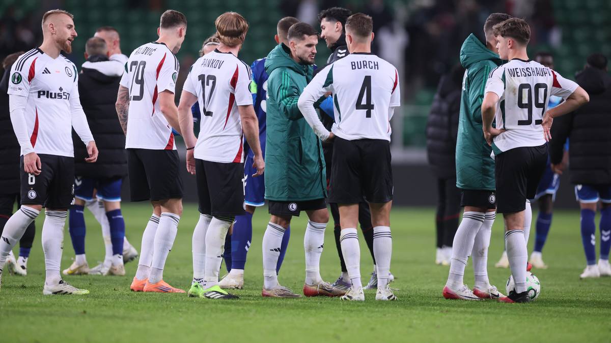 Grupa piłkarzy w białych i zielonych strojach stojąca na boisku.