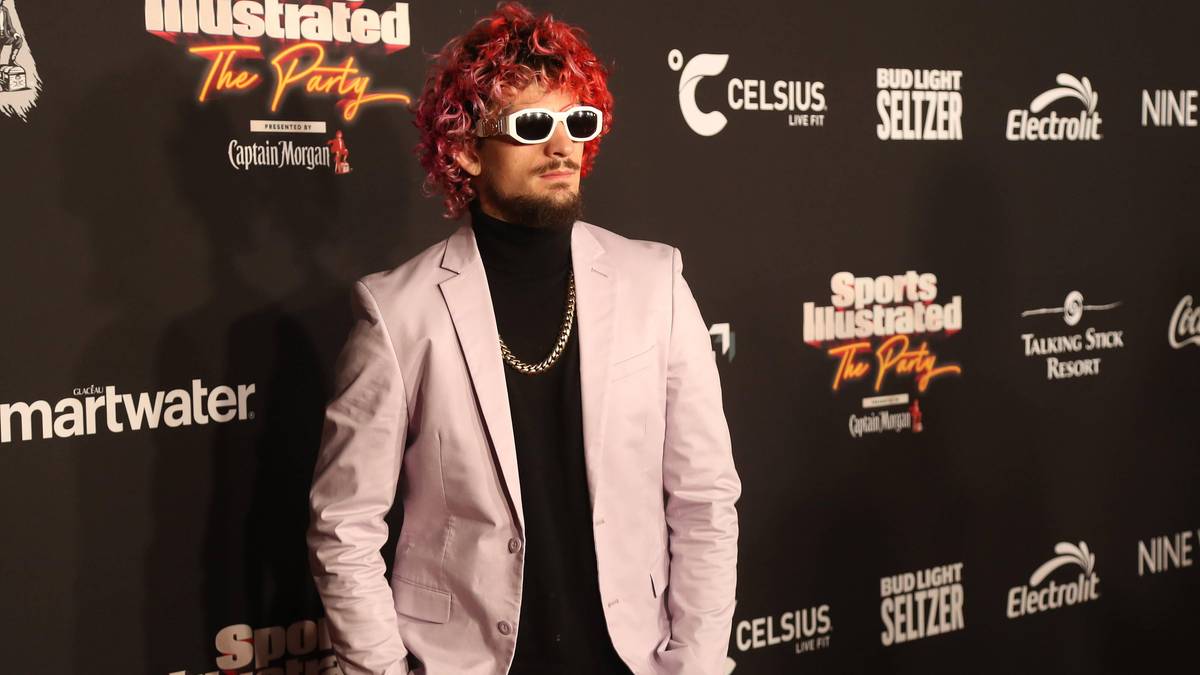 Sean O'Malley, zawodnik MMA, ubrany w jasnor&oacute;żowy garnitur, czarną golf i białe okulary przeciwsłoneczne.