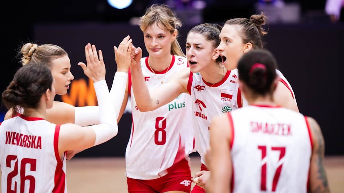 Pięć siatkarek w białych koszulkach z czerwonymi elementami, z numerami na plecach, w otwartym geście współpracy i entuzjazmu, patrzą w tym samym kierunku.