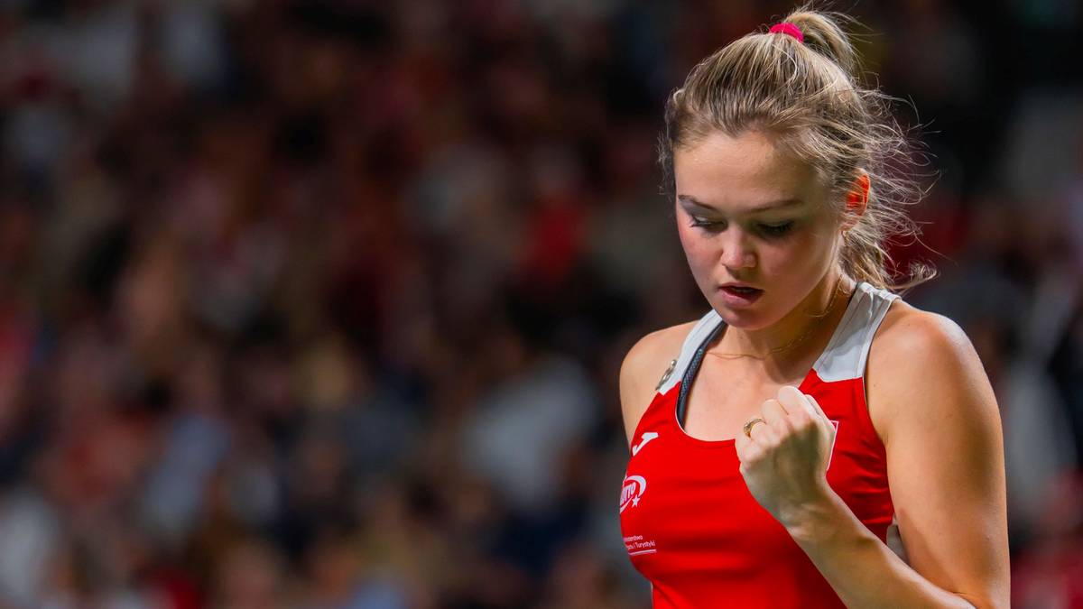 Młoda kobieta w czerwonym stroju tenisowym, z zaciśniętą prawą pięścią, patrząca z determinacją.