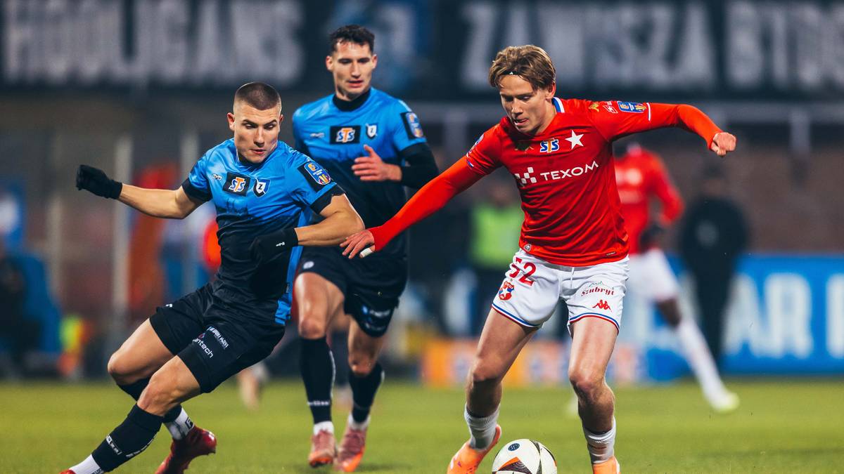 Dwóch piłkarzy walczących o piłkę na boisku, jeden w czerwonej koszulce, drugi w niebiesko-czarnej.