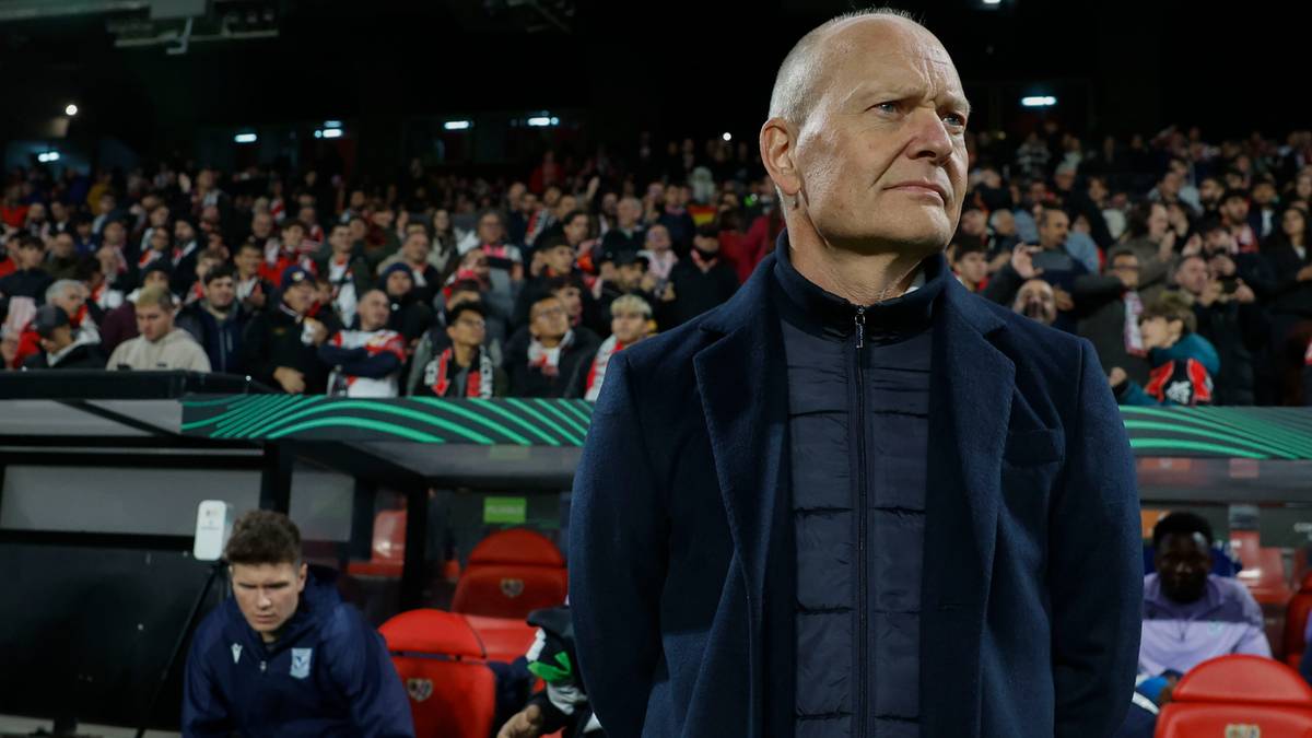 Trener drużyny piłkarskiej stoi na tle trybun.