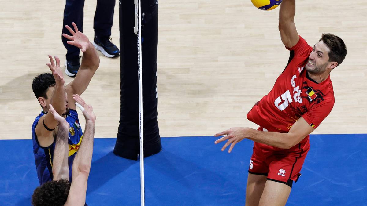 Siatkarz w czerwonej koszulce wykonuje zagrywkę, a przeciwnik w niebieskiej koszulce pr&oacute;buje go zablokować.