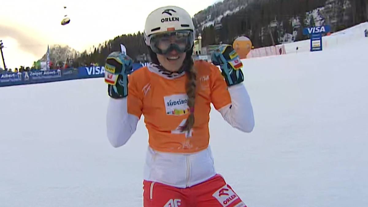 Snowboarderka Aleksandra Kr&oacute;l-Walas w kasku i goglach, ubrana w pomarańczową bluzę sportową i białą kurtkę, z uśmiechem pokazuje kciuki w g&oacute;rę.