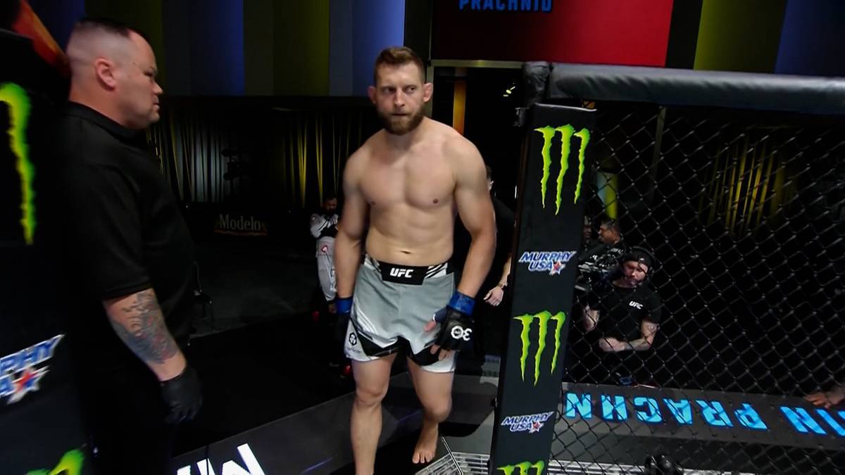 Zawodnik MMA w szortach i rękawicach bokserskich wychodzi na ring, obok stoi ochroniarz.