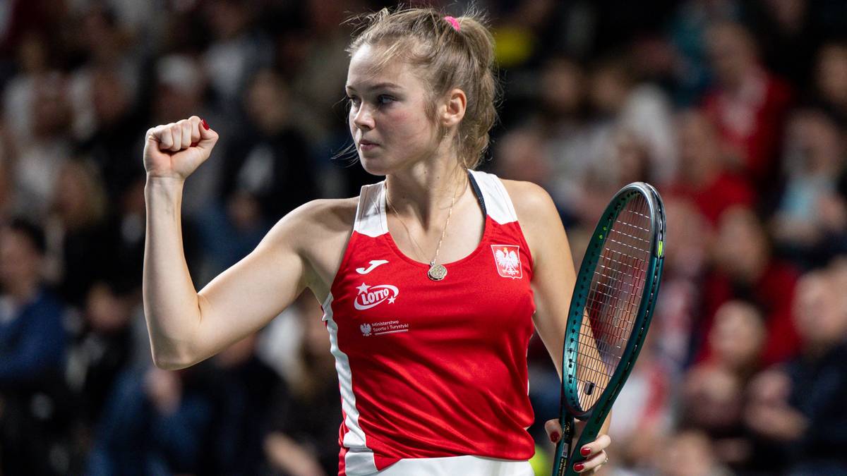 Tenisistka w biało-czerwonym stroju z podniesioną pięścią i rakietą tenisową.