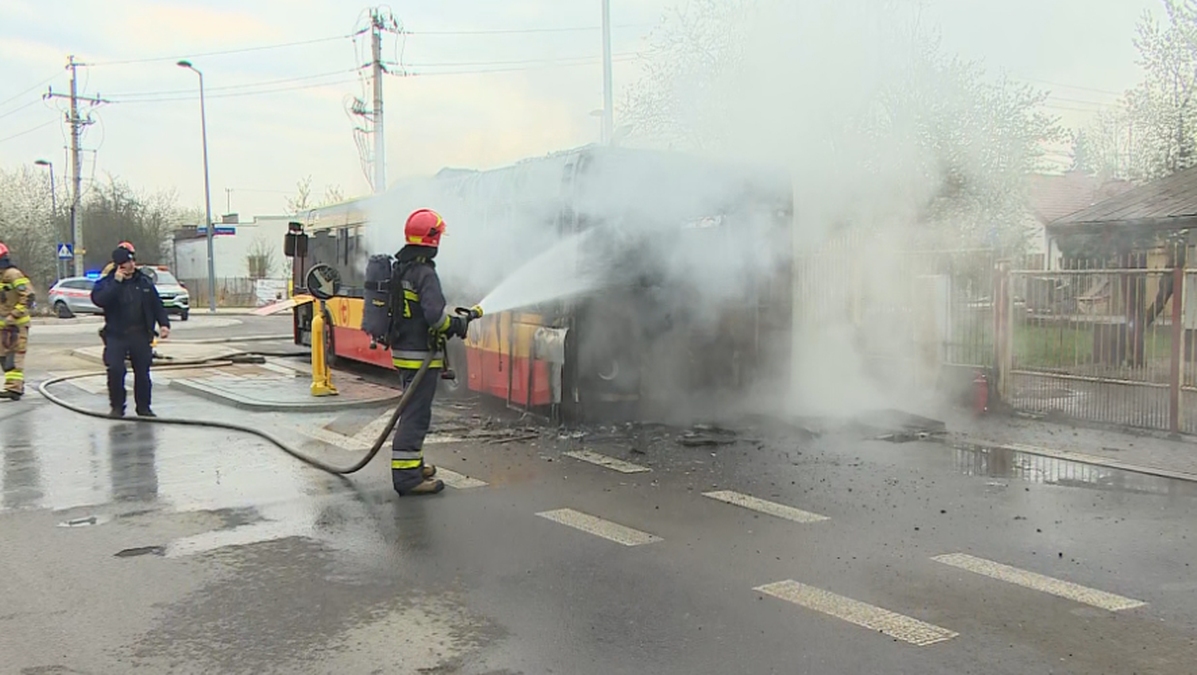 Strażacy gaszą płonący autobus, z pojazdu wydobywa się gęsty dym.