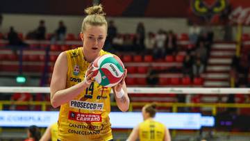 Siatkarka w ż&oacute;łtym stroju z piłką w rękach przygotowuje się do zagrywki na hali sportowej.