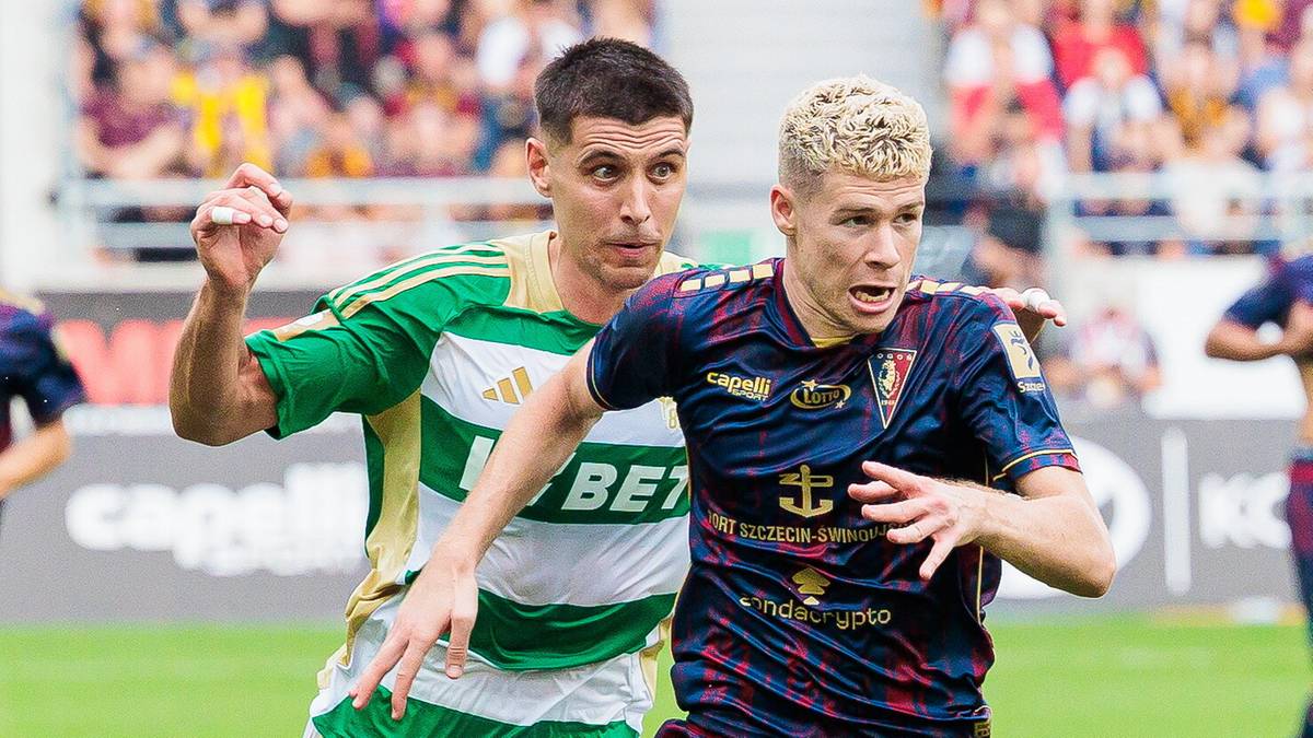 Dwóch piłkarzy w akcji podczas meczu piłki nożnej, jeden w zielono-białej koszulce, drugi w granatowo-czerwonej koszulce.