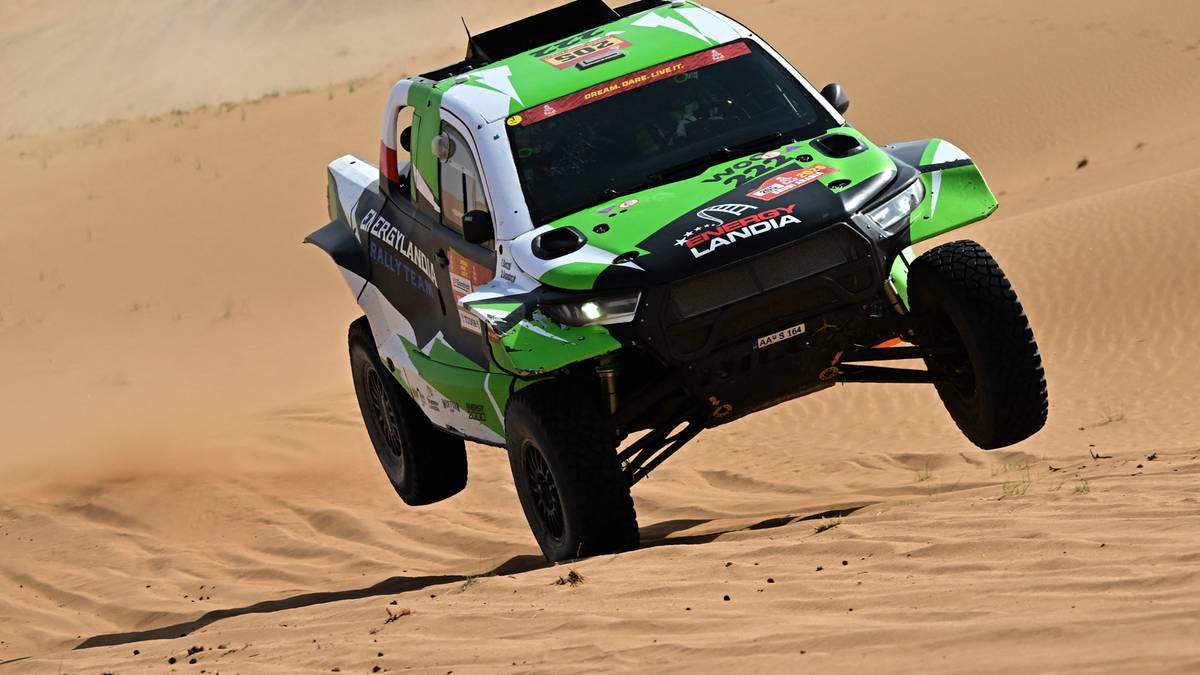 Zielono-biały samoch&oacute;d rajdowy jadący po piaszczystym terenie.