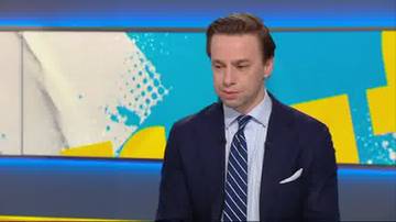 Mężczyzna w garniturze i krawacie siedzi przed kolorowym, geometrycznym tłem.