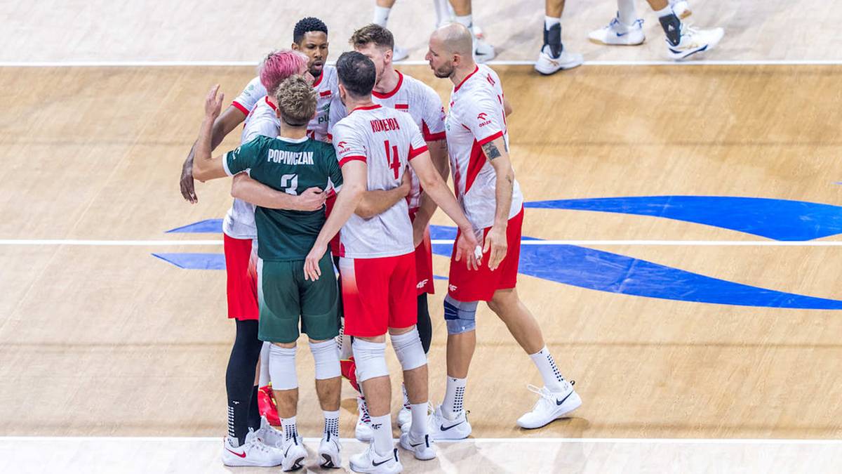 Grupa siatkarzy w białych i zielonych strojach sportowych przytulających się na boisku siatkarskim.