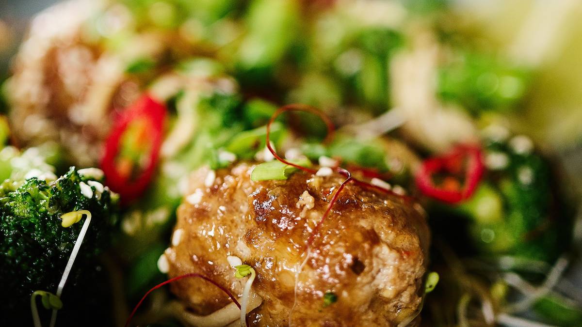 Miseczka z daniem zawierającym brokuły, kawałki mięsa lub tofu w panierce z sezamu, makaron i plasterki chili.