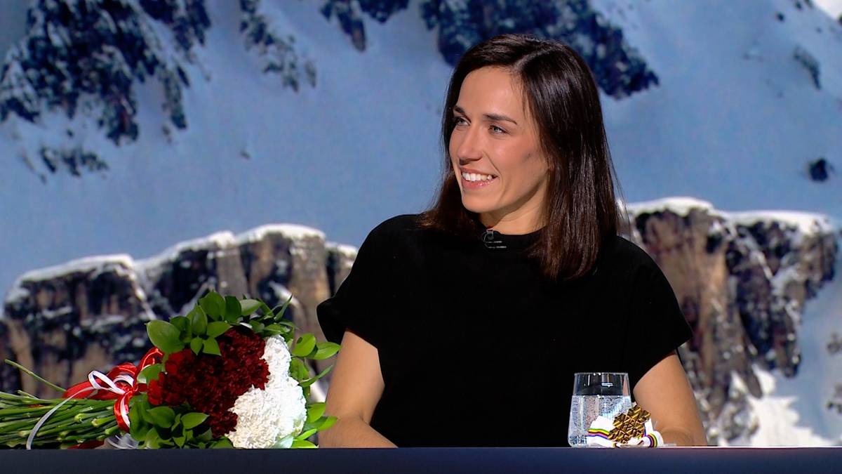 Kobieta z bukietem kwiat&oacute;w i szklanką wody, siedząca przed ekranem z zimowym krajobrazem.