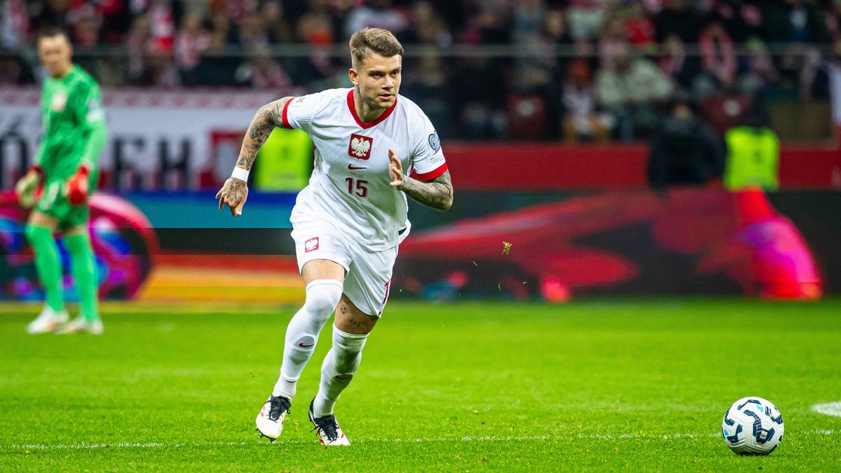 Piłkarz w białej koszulce reprezentacji Polski z numerem 15 na plecach biegnie z piłką po boisku.