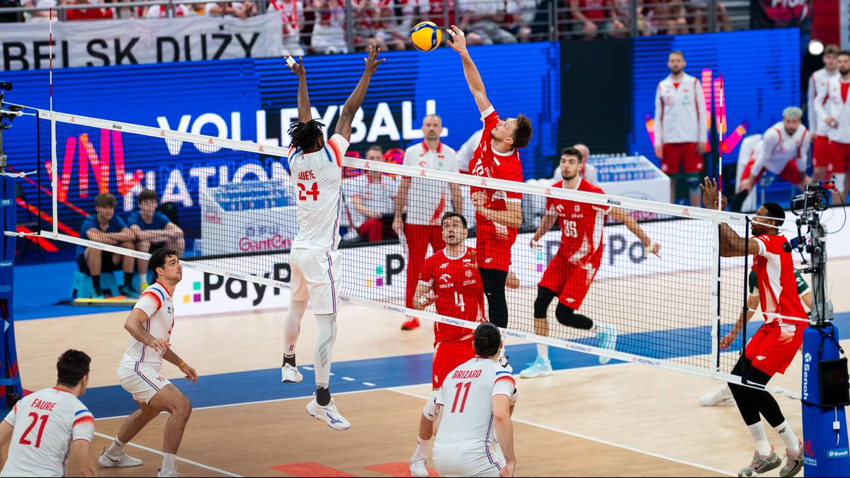 Siatkarze w akcji przy siatce podczas meczu z udziałem licznych kibiców na trybunach.