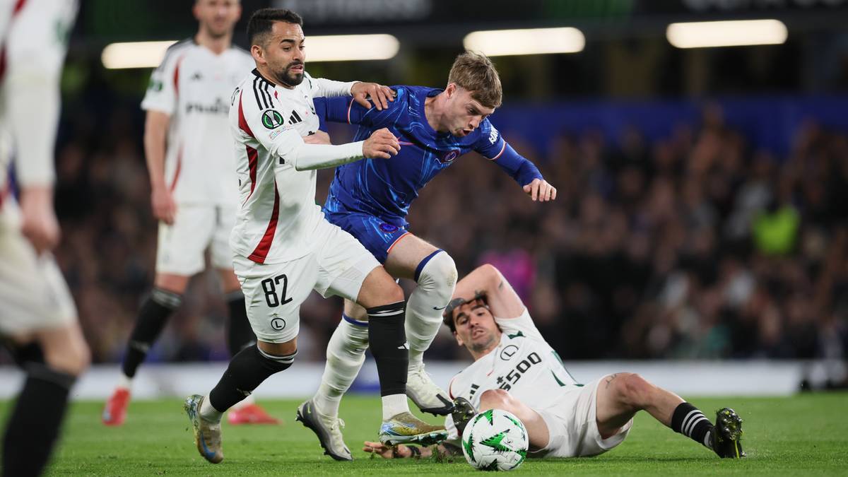 Trzech piłkarzy w akcji podczas meczu. Jeden w białej koszulce z numerem 82, dwóch w niebieskiej i białej koszulce.