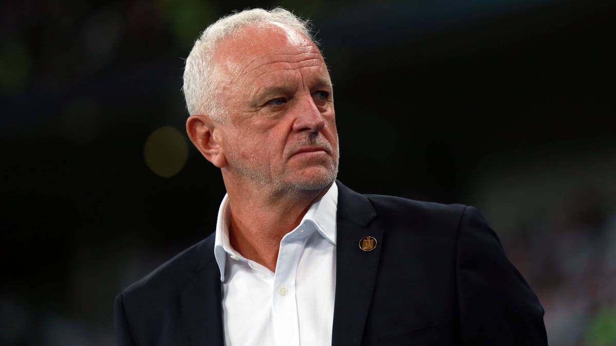 Portret trenera piłkarskiego z siwymi włosami, ubranego w białą koszulę i marynarkę, patrzącego w bok.