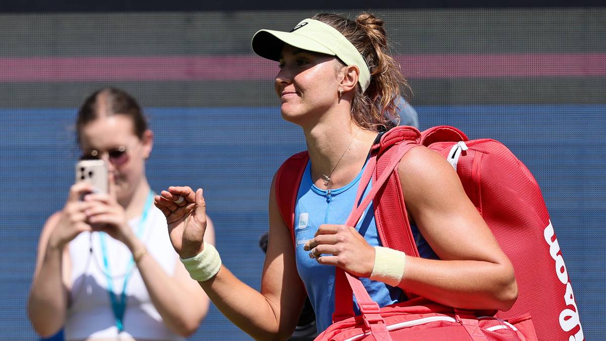 Tenisistka w czapce z daszkiem i niebieskim stroju sportowym niesie czerwony plecak na ramieniu.