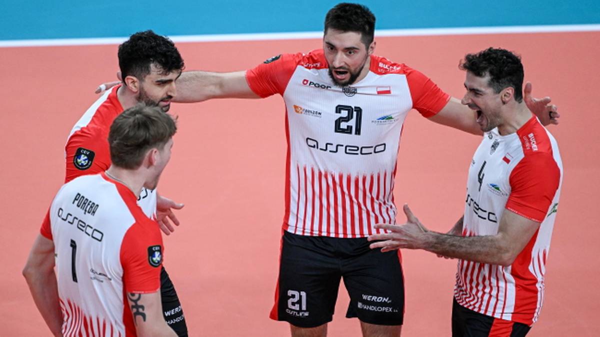 Czterech siatkarzy w białych i czerwonych koszulkach świętuje na boisku siatkarskim.