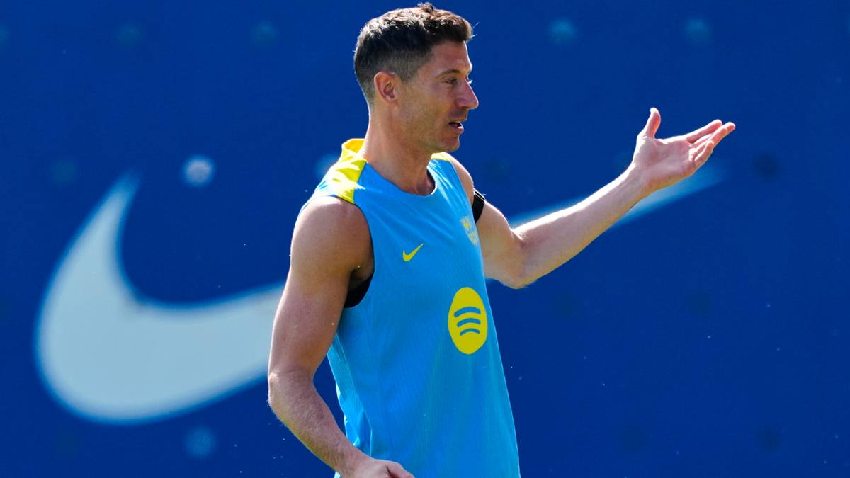 Piłkarz Robert Lewandowski w niebieskiej koszulce treningowej z ż&oacute;łtym kołnierzem, gestykuluje prawą ręką.