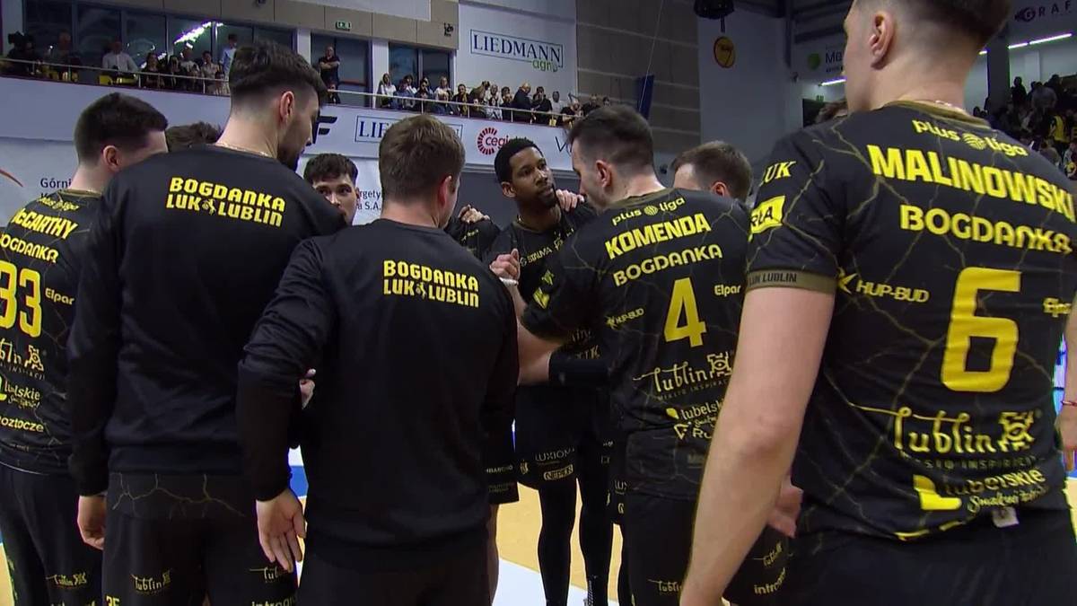 Grupa siatkarzy w czarnych strojach z żółtymi napisami stoi w kółku podczas odprawy taktycznej.