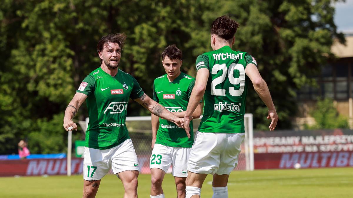 Trzech piłkarzy w zielonych koszulkach z numerami 17, 23 i 29 na boisku piłkarskim.