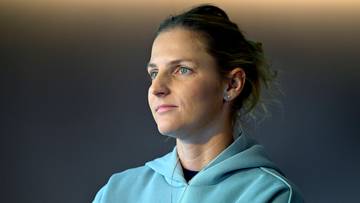 Karolina Pliskova w jasnoniebieskiej bluzie z kapturem, patrząca w bok z zamyślonym wyrazem twarzy.