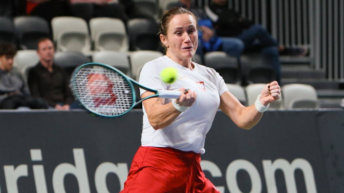 Tenisistka w białej koszulce i czerwonej spódniczce uderza piłkę rakietą podczas meczu.