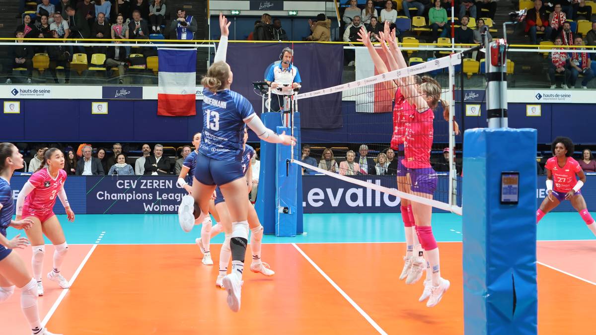 Siatkarki w akcji podczas meczu Ligi Mistrzyń, jedna próbuje zablokować atak przeciwniczki nad siatką.