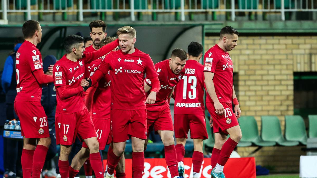 Piłkarze w czerwonych strojach celebrują gola, stojąc blisko siebie na boisku.