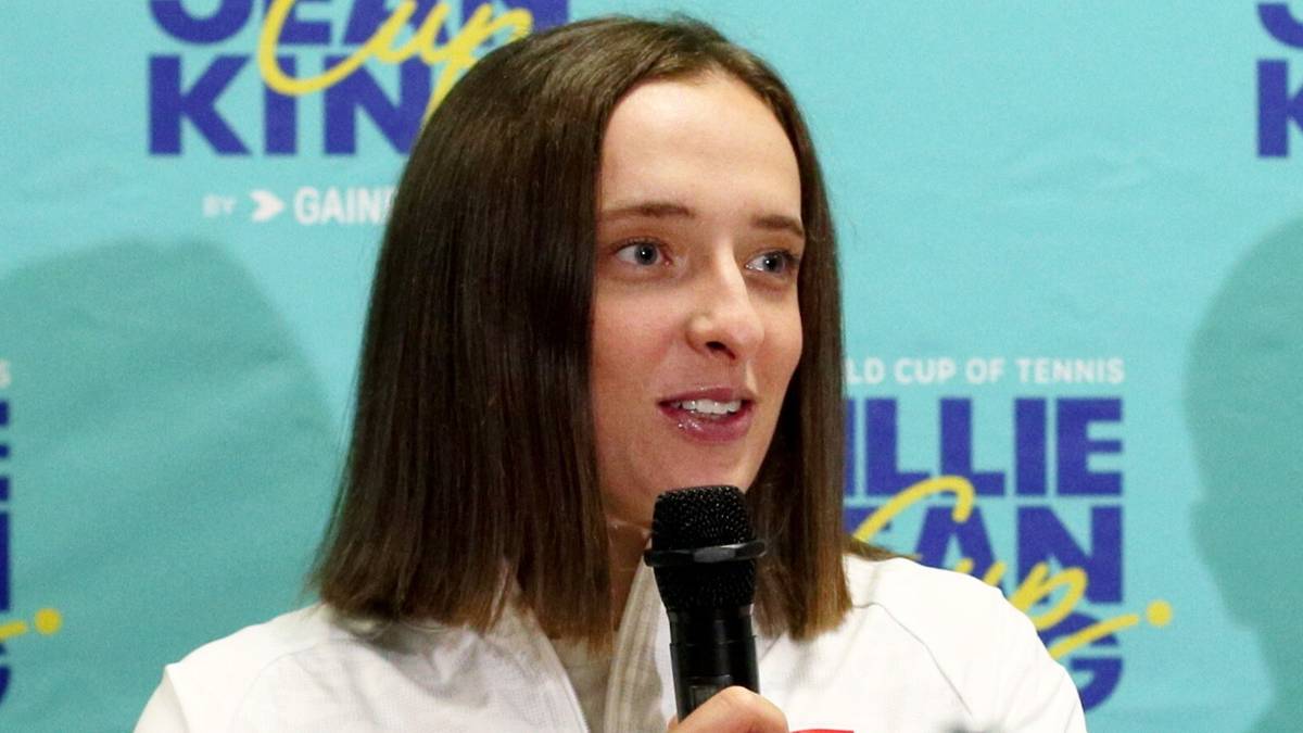 Iga Świątek przemawia podczas konferencji prasowej, siedząc przy stole z innymi osobami.