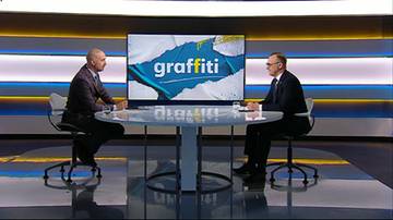 Dw&oacute;ch mężczyzn siedzących przy okrągłym stole w studiu telewizyjnym, naprzeciwko siebie. Za nimi znajduje się duży ekran z logo "graffiti".