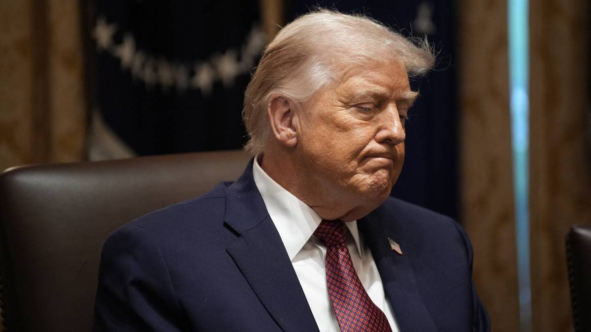 Donald Trump w garniturze i krawacie, siedzący w pomieszczeniu, patrzący w bok z lekko zamyśloną miną.