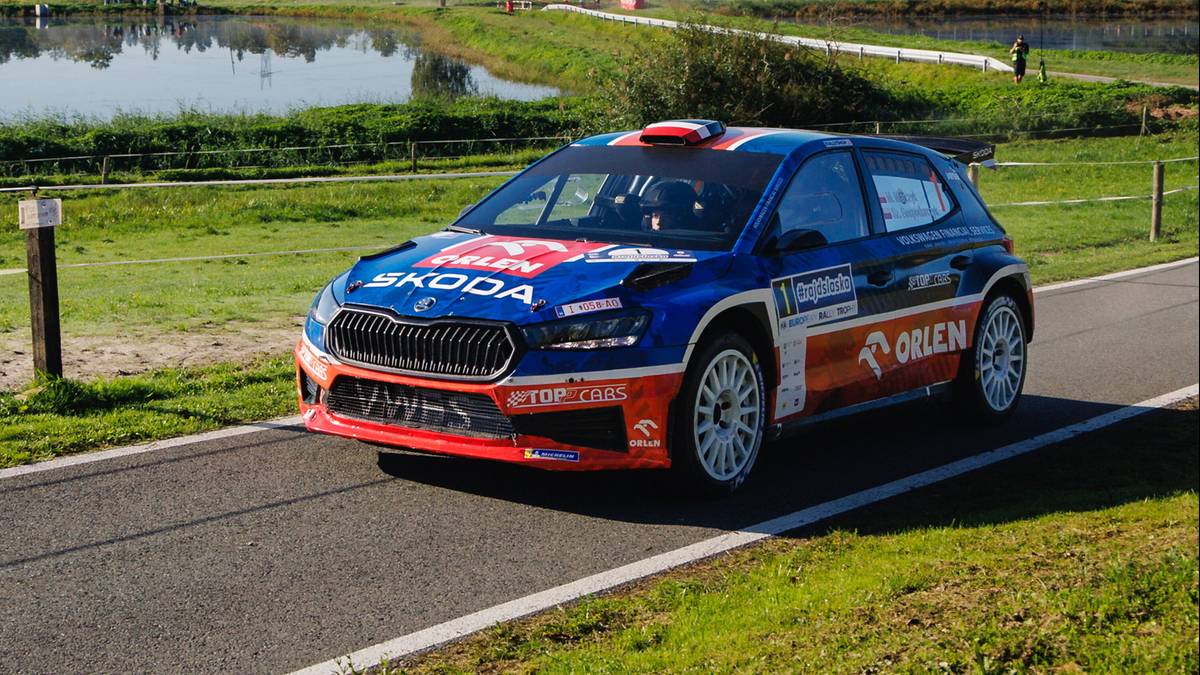 Samochód rajdowy Skoda Fabia w barwach ORLEN i SKODA, z numerem startowym 1, przejeżdża po asfaltowej drodze. Samochód ma na drzwiach napisy "Marczyk" i "Gospodarczyk".