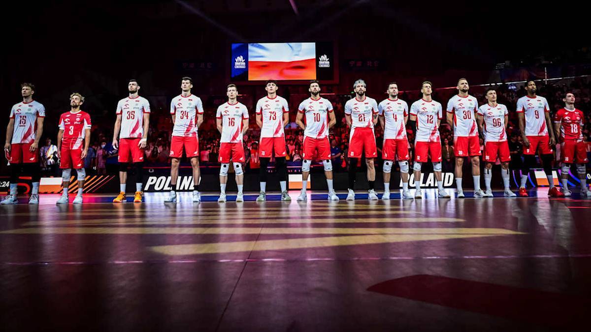 Drużyna siatkarska w strojach sportowych stoi w rzędzie na boisku.