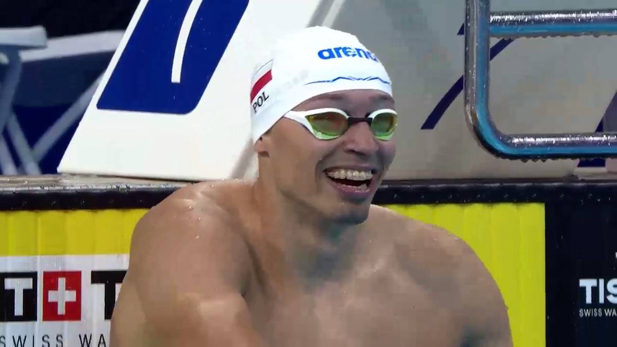 Uśmiechnięty pływak w białym czepku z napisem POL i w goglach pływackich.