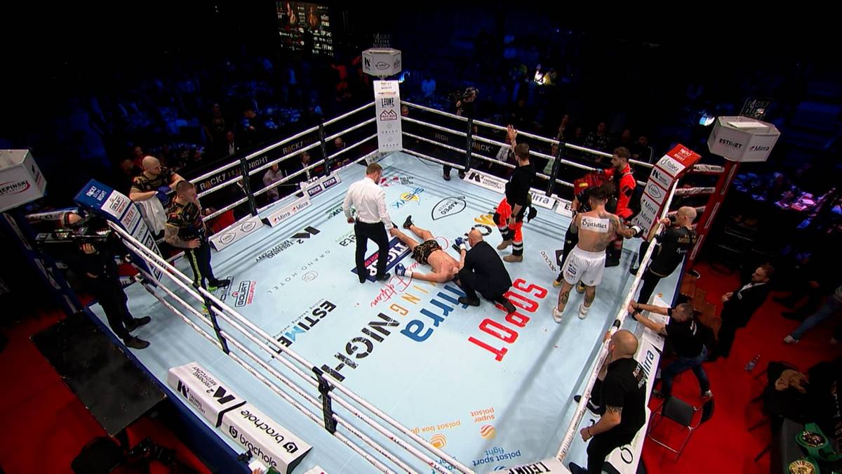 Ring bokserski z leżącym zawodnikiem, wokół którego zgromadziły się osoby.