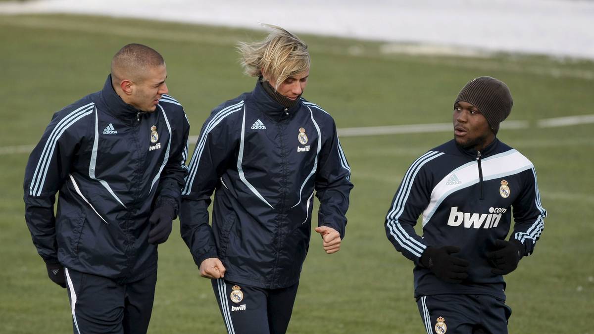 Trzech piłkarzy Realu Madryt w kurtkach treningowych idzie po boisku.