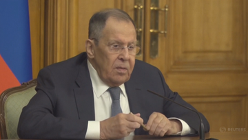 Siergiej Ławrow w garniturze i krawacie siedzi przy stole, m&oacute;wiąc do mikrofonu.