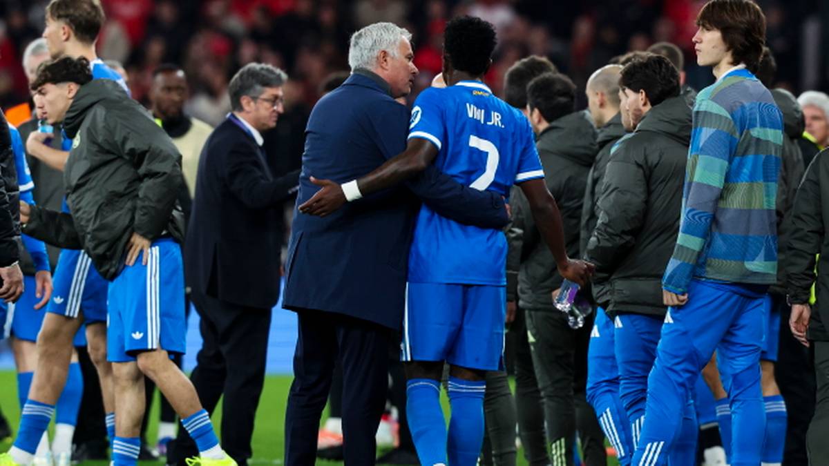 Jose Mourinho w płaszczu rozmawia z piłkarzem w niebieskiej koszulce z numerem 7 na plecach, otoczeni przez innych zawodnik&oacute;w.