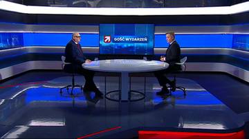 Dw&oacute;ch mężczyzn w garniturach siedzi przy okrągłym stole w studiu telewizyjnym.