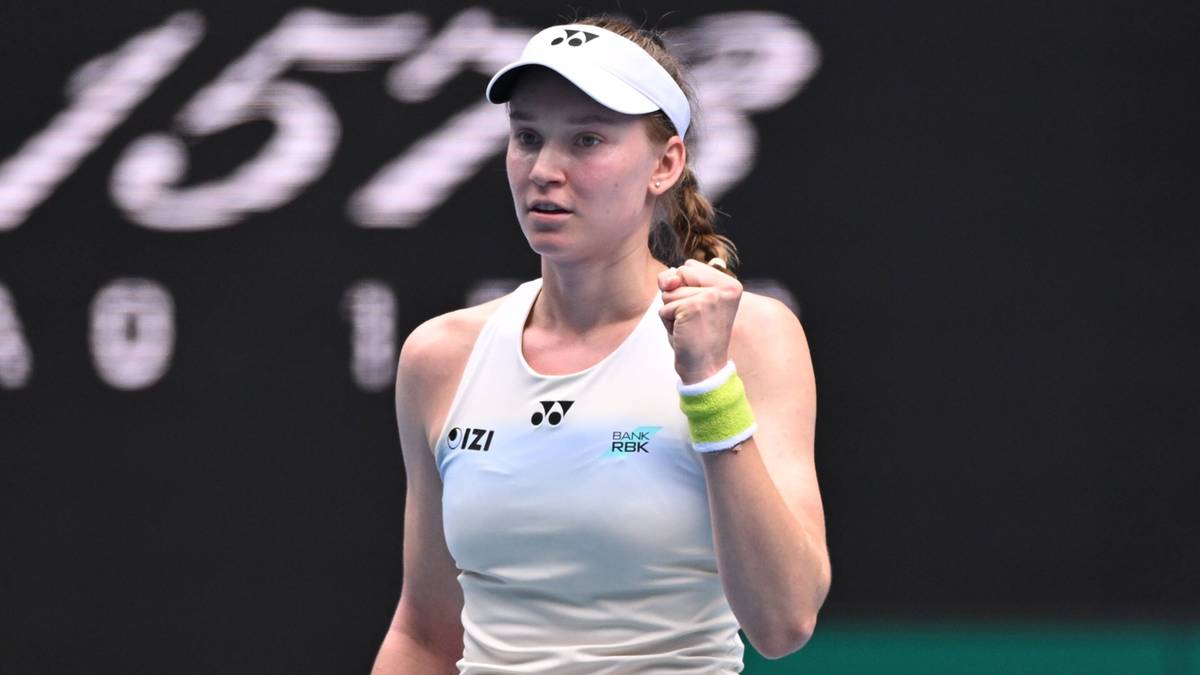 Jelena Rybakina w białym stroju sportowym i czapce z daszkiem, z zaciśniętą pięścią uniesioną w geście triumfu.